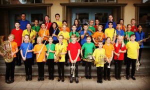 Die Stadtkapelle Wernau versammelt junge Musiker in farbenfrohen T-Shirts und spielt verschiedene Blasinstrumente auf den Treppen vor ihrem Probenraum. Fördernde Gemeinschaft und musikalische Bildung im Landkreis Esslingen und Stuttgart stehen im Fokus.