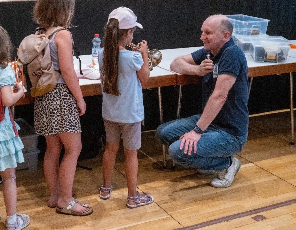 Bild einer Musikerinteraktion mit Kindern bei der Stadtkapelle Wernau, die Interesse an Musik im Landkreis Esslingen und Stuttgart weckt. Musiker zeigt Kindern Blasinstrumente, ideal für Familien und Musikliebhaber.