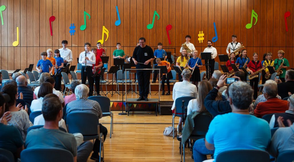 Auftritt der Stadtkapelle Wernau mit jugendlichen Musikern, die verschiedene Instrumente spielen. Die Veranstaltung in einem großen Saal zieht zahlreiche Zuschauer an und fördert das musikalische Interesse in der Region Esslingen und Stuttgart.