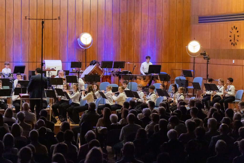 Auftritt der Stadtkapelle Wernau während eines Konzerts mit begeistertem Publikum, das talentierte Musiker aus dem Raum Esslingen und Stuttgart präsentiert. Die Aufführung zeigt verschiedene Instrumente und junge Musiker in festlicher Kleidung, die gemeinsam musizieren.