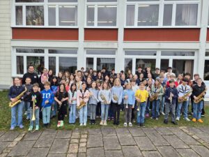 Gruppenfoto der Stadtkapelle Wernau mit jungen Musikern, die verschiedene Blasinstrumente halten, vor einem Gebäude. Die Aufnahme spricht Musiker und Musikliebhaber im Raum Esslingen und Stuttgart an und fördert musikalische Aktivitäten im Landkreis.