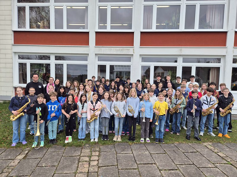 Gruppenfoto der Stadtkapelle Wernau mit jungen Musikern, die verschiedene Blasinstrumente halten, vor einem Gebäude. Die Aufnahme spricht Musiker und Musikliebhaber im Raum Esslingen und Stuttgart an und fördert musikalische Aktivitäten im Landkreis.