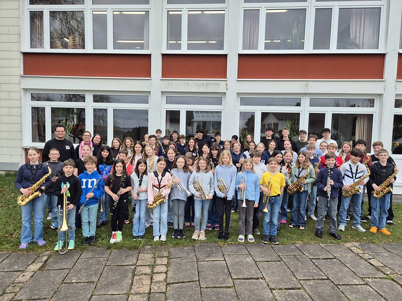 Gruppenfoto der Stadtkapelle Wernau mit jungen Musikern, die verschiedene Blasinstrumente halten, vor einem Gebäude. Die Aufnahme spricht Musiker und Musikliebhaber im Raum Esslingen und Stuttgart an und fördert musikalische Aktivitäten im Landkreis.